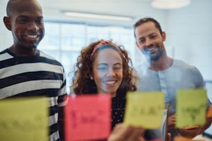 Group of diverse designers reading sticky notes on a glass wall during a brainstorming session in an modern office