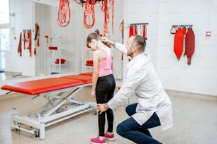 Fisioterapeuta mirando la espalda de la niña durante el examen médico en la oficina de rehabilitación con equipo médico suspendido