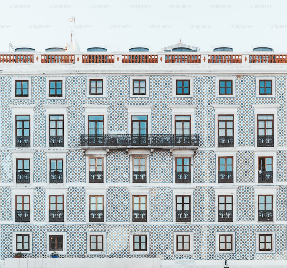 Fachada de uma casa regular em Portugal revestida de azulejos, com uma longa varanda no centro; textura de uma elevação de um edifício residencial comum em Lisboa com muitas janelas