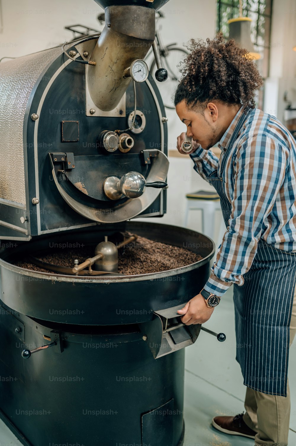 Mixed race barista checking the quality of roasted coffee beans standing near the roaster machine at the coffee shop