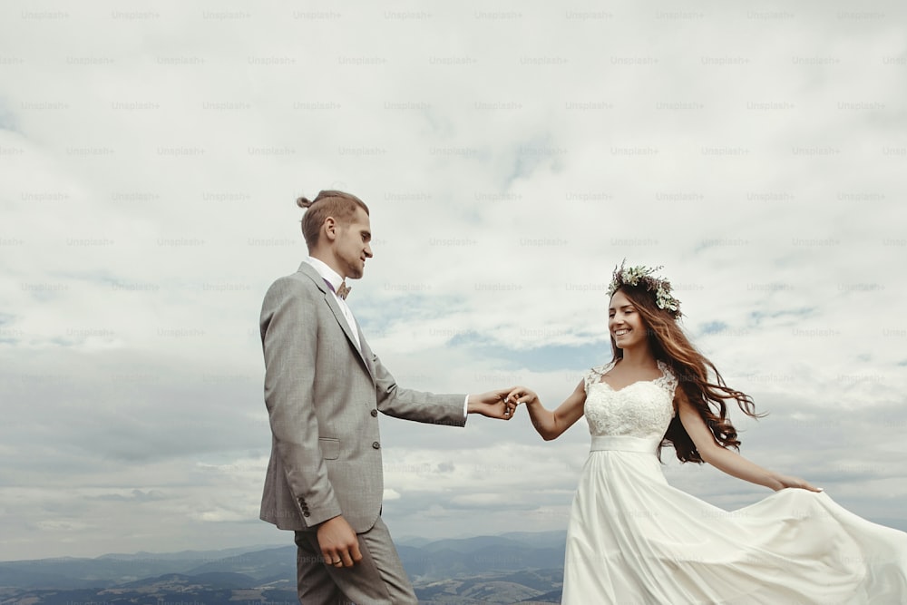 lindos noivos de mãos dadas e dançando no céu e nas nuvens, momento de verdadeira felicidade, cerimônia de luxo nas montanhas com vista incrível, espaço para texto