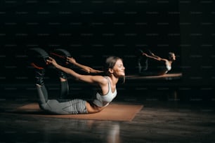 Beautiful Caucasian brunette lying down on stomach on mat and stretching while wearing exercise footwear.