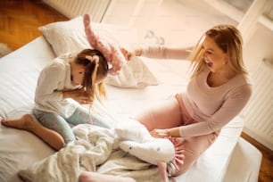 Funny mornings. Mother and daughter having pillow fight in bed.