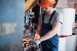 Porträt eines jungen Arbeiters mit Schutzhelm in einer großen Müllrecyclingfabrik. Der Ingenieur überwacht die Arbeit von Maschinen und anderen Geräten.