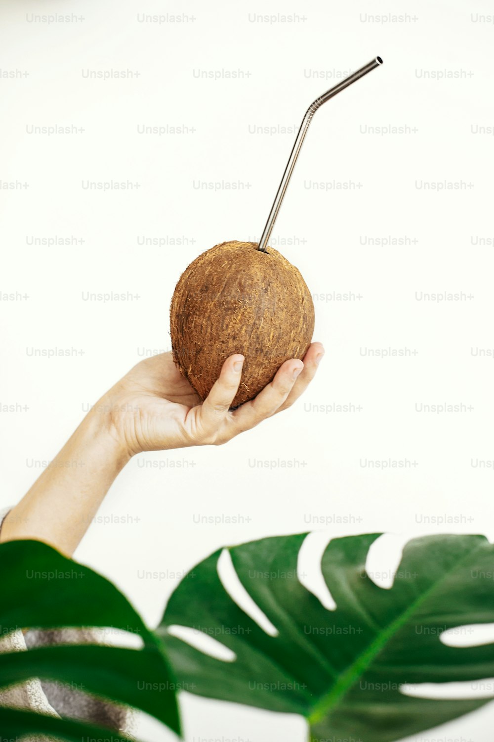 Hand holding coconut with metal straw on white background with green palm leaves. Hello summer vacation concept. Zero waste.  Ban plastic. Sustainable lifestyle on tropical island. Copy space