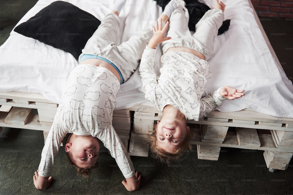 Des enfants heureux jouant dans une chambre noire. Petit garçon et petite fille, frère et sœur jouent sur le lit en pyjama.