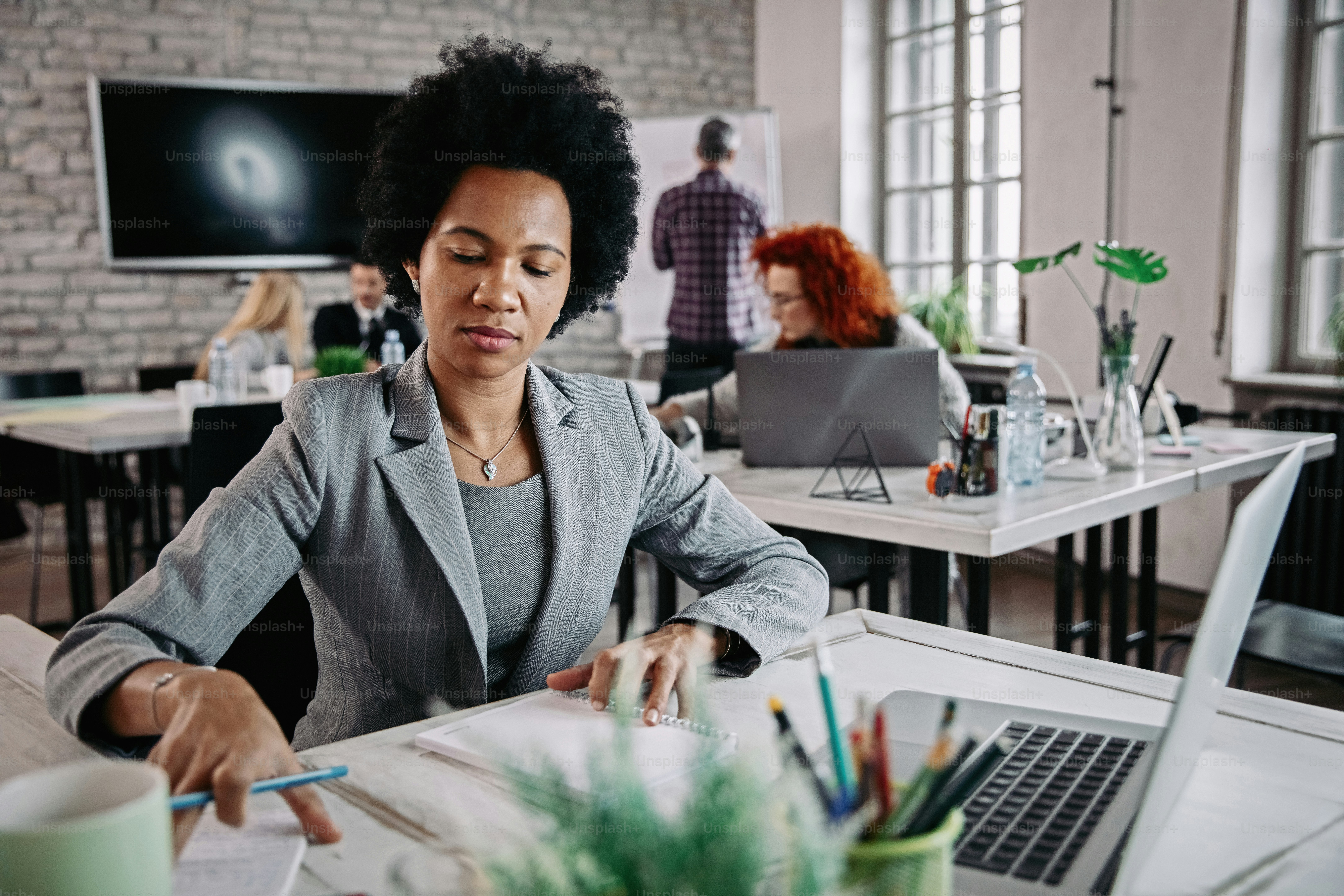 African American businesswoman working on paperwork while being at work in corporate office. There are people in the background.