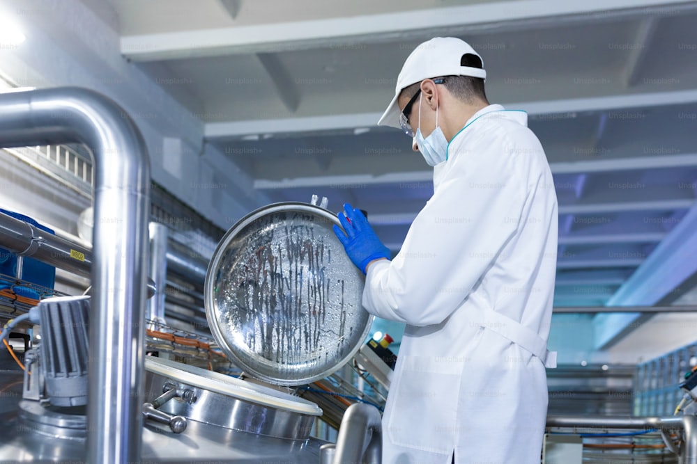 Technologist in a cap, mask and white coat is in the production shop. inspector removes the indicators at the dairy plant. Engineer keeps statistics on production