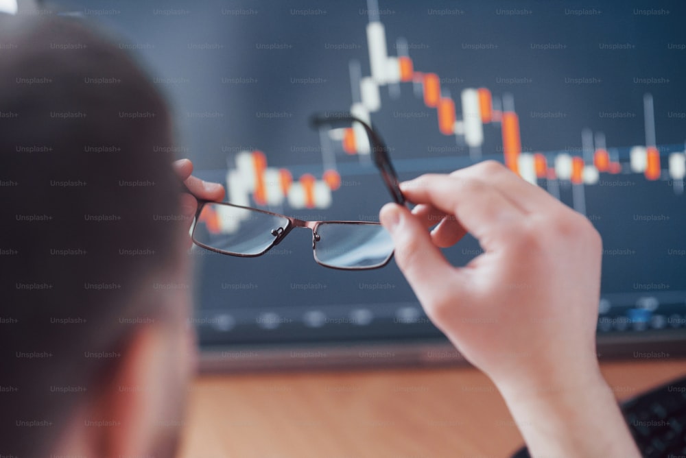 Analyzing data. Close up of a young businessman who holds glasses and looks at the gff while working in a creative office.