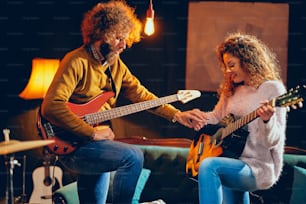 Kaukasische Frau spielt akustische Gitarre, während Mann Bass spielt. Home Studio Interieur.