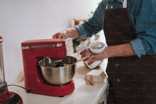 Man cooking in the kitchen and putting sugar from the jar into the bowl of electric stand mixer