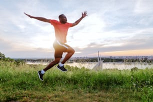 自然の中で速く走るスポーツウェアを着たハンサムなアフリカ系アメリカ人の男。背景の都市、川、橋。私は自分の人生に日数を足すために走るのではなく、日々に命を吹き込むために走るのです。