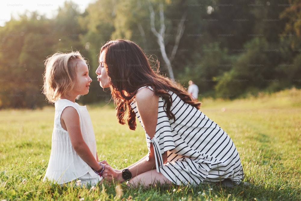 Madre e figlia felici che si abbracciano in un parco al sole su uno sfondo estivo luminoso di erbe