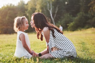 Happy mother and daughter hugging in a park in the sun on a bright summer background of herbs