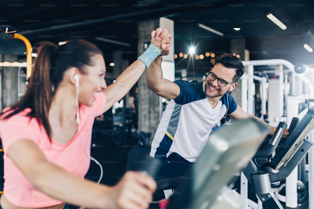 Young and attractive woman and man biking in the fitness gym. They exercising legs and doing cardio workout while riding cycling machines.