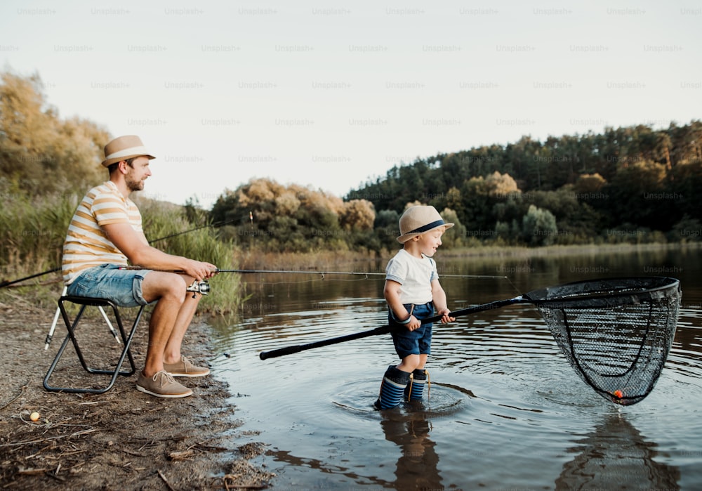A mature father with a small toddler son outdoors fishing by a river or a lake.