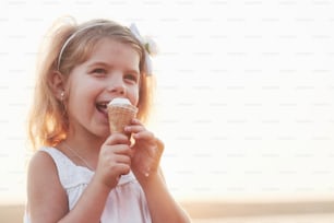 Bambina sorridente carina che mangia il gelato sullo sfondo del lago e dei boschi.