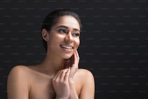 Portrait of young woman with undressed upper body having shy expression. Copy space in right side. Isolated on black background
