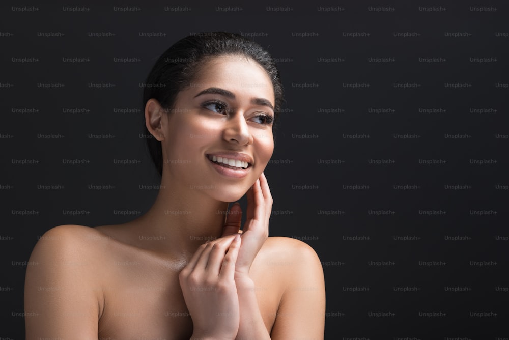 Portrait of young woman with undressed upper body having shy expression. Copy space in right side. Isolated on black background