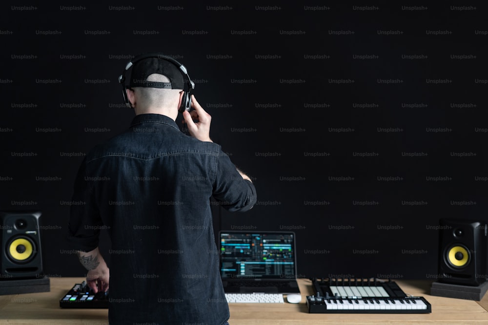 Rear back behind view of unrecognizable creativity DJ man in headset using controller and making music in sound recording studio with copy empty space for text