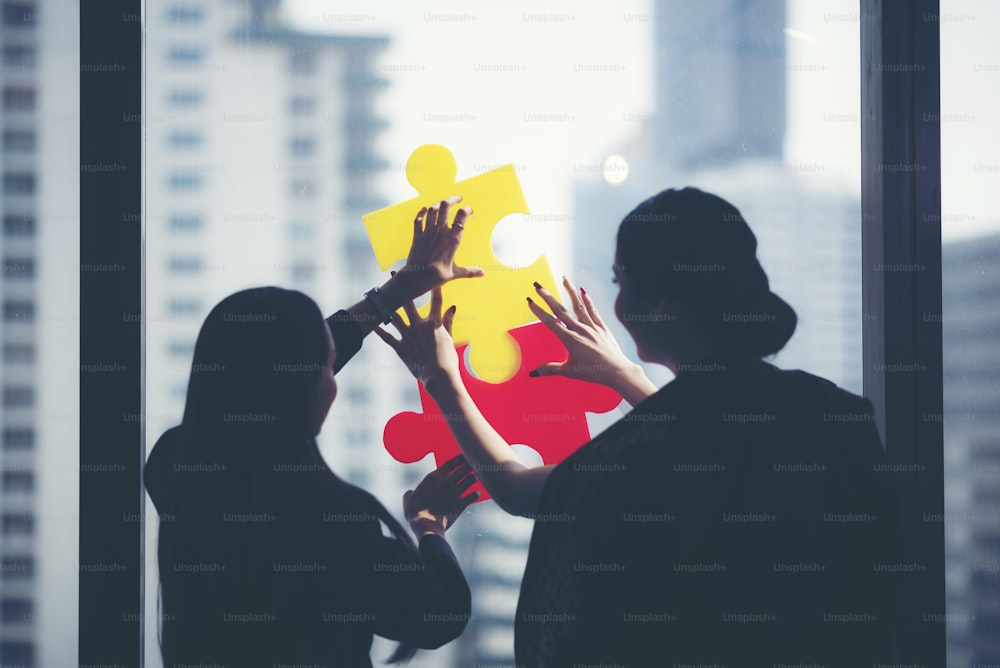 two businesswomen trying to connect couple puzzle piece with city sunset background, one part of whole. symbol of association and connection. business strategy