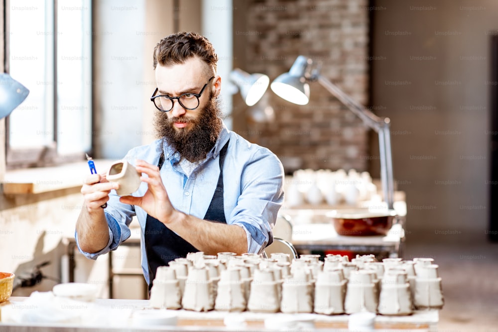 Bel homme barbu travaillant avec des pièces en céramique sur le lieu de travail dans l’atelier de poterie
