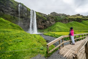 Mulher viajante na cachoeira mágica Seljalandsfoss na Islândia localizada perto do anel viário do sul da Islândia. Majestoso e pitoresco, é um dos lugares de tirar o fôlego mais fotografados do deserto da Islândia
