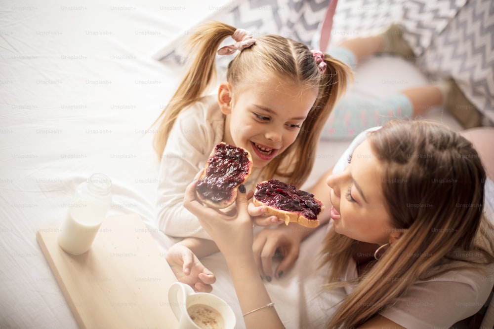 Share breakfast. Mother and daughter having breakfast in bed.