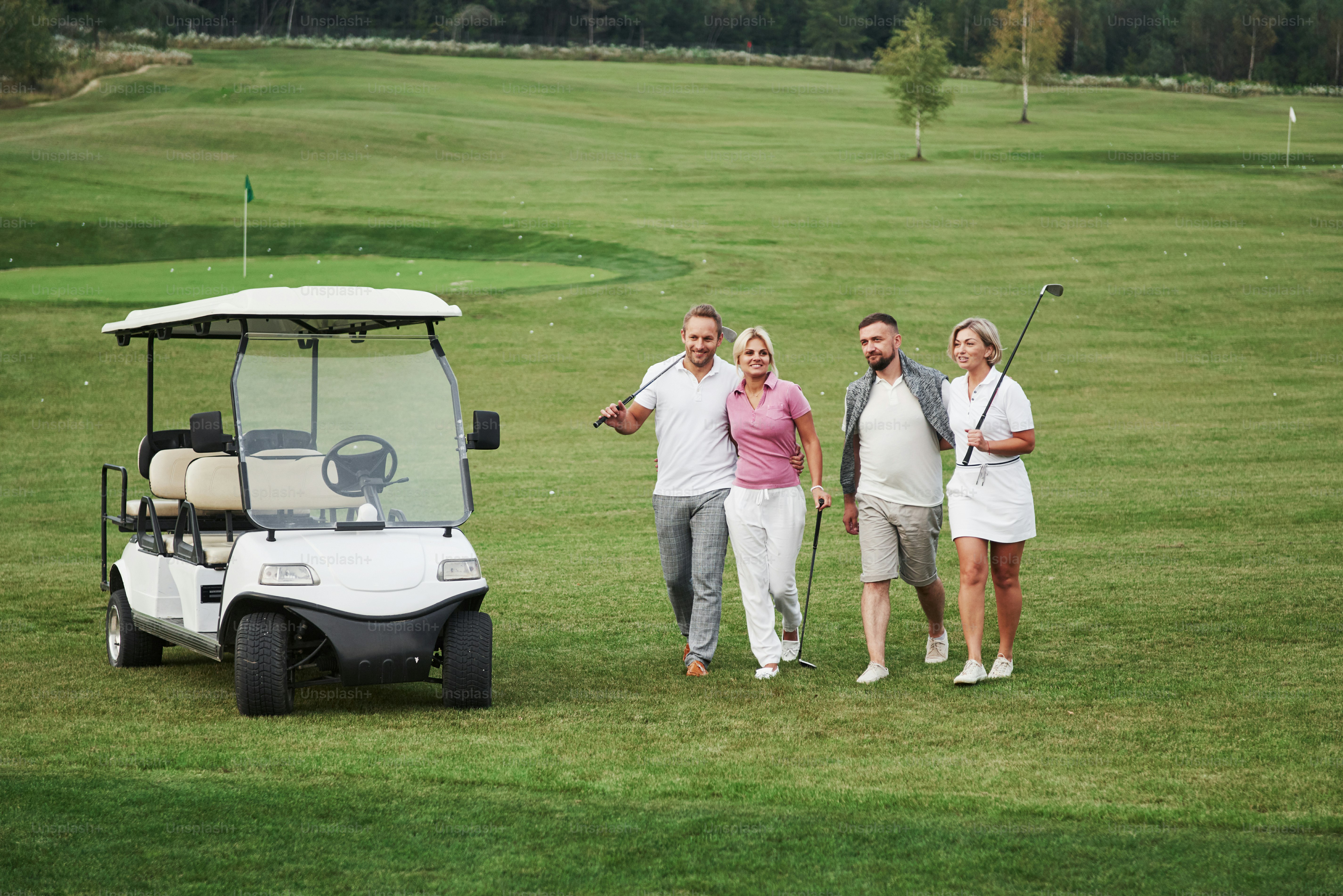 Young couples getting ready to play. A group of smiling friends came to the hole on a golf cart.