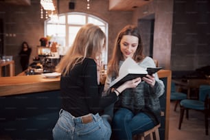 Dos mujeres jóvenes sentadas en la cafetería tomando café y disfrutando de buenos libros. Estudiantes en la pausa del café. Educación, concepto de estilo de vida.