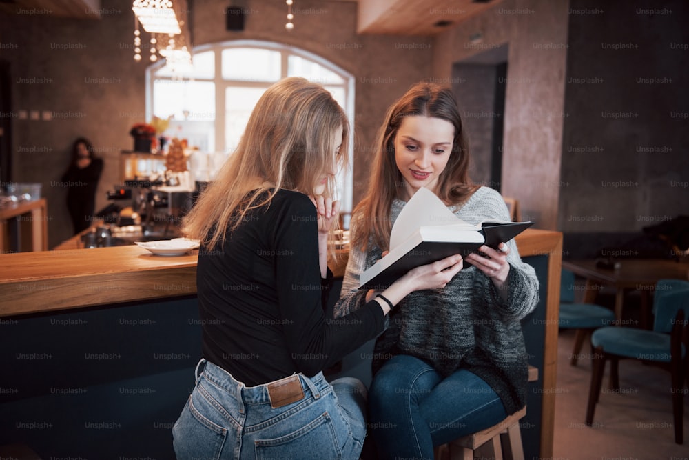 Due giovani donne sedute nel bar che bevono caffè e si divertono in buoni libri. Studenti in pausa caffè. Educazione, concetto di stile di vita.