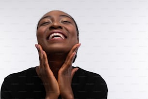 Sorrindo amplamente. Mulher afro-americana radiante e bonita tocando seu rosto enquanto sorri amplamente