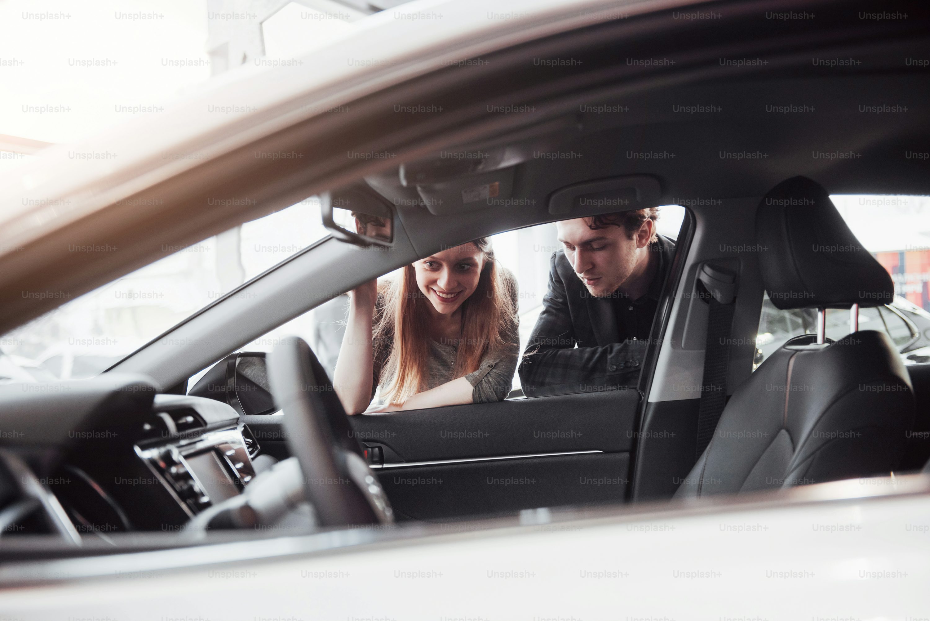 I like this car. Beautiful young couple standing at the dealership choosing the car to buy.