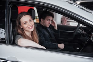 Proud owners. Beautiful young happy couple hugging standing near their newly bought car smiling joyfully showing car keys to the camera copyspace family love relationship lifestyle buying consumerism.