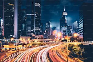 夜の香港の街路交通。オフィスビル、高層ビル、ぼやけた車、光の軌跡のある高速道路の交通量が多い。香港、中国