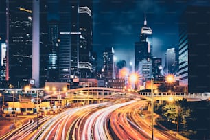 Street traffic in Hong Kong at night. Office skyscraper buildings and busy traffic on highway road with blurred cars light trails. Hong Kong, China