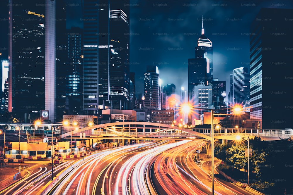 Straßenverkehr in Hongkong bei Nacht. Büro-Wolkenkratzergebäude und reger Verkehr auf der Autobahnstraße mit verschwommenen Autos Lichtspuren. Hongkong, China
