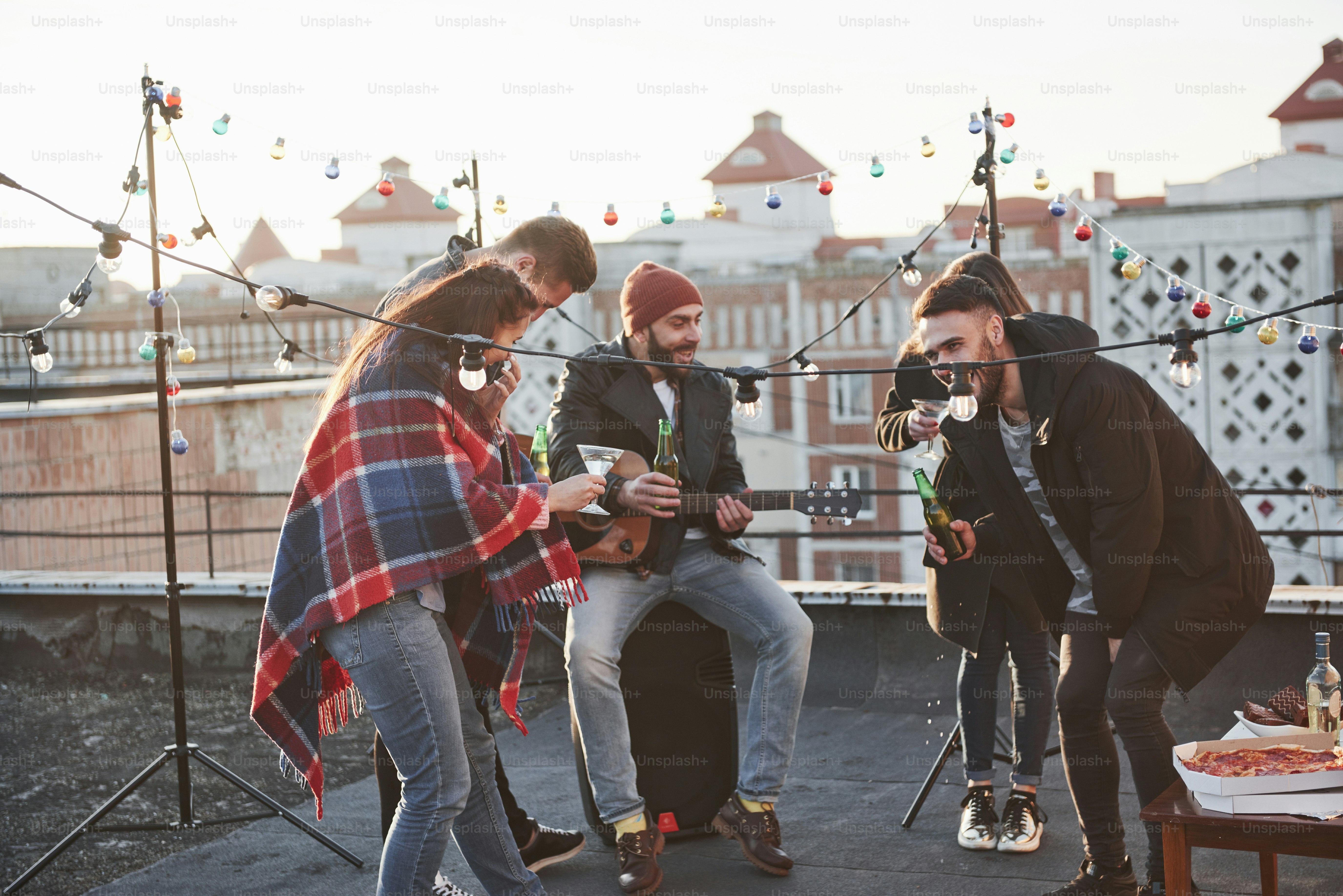 Cinco jóvenes amigos tienen una fiesta con cerveza y guitarra en la azotea.