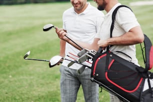 Avoir une conversation et sourire. Photo recadrée de deux amis sur le terrain de sport avec de l’équipement de golf.