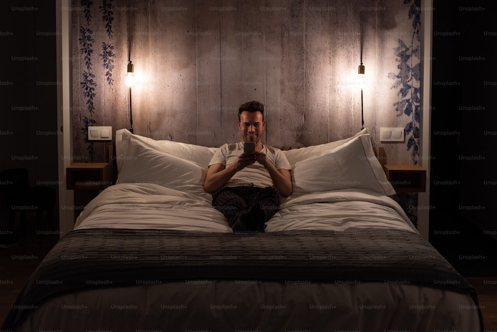 Man on the mobile phone lying down in bed in a modern beautiful bedroom