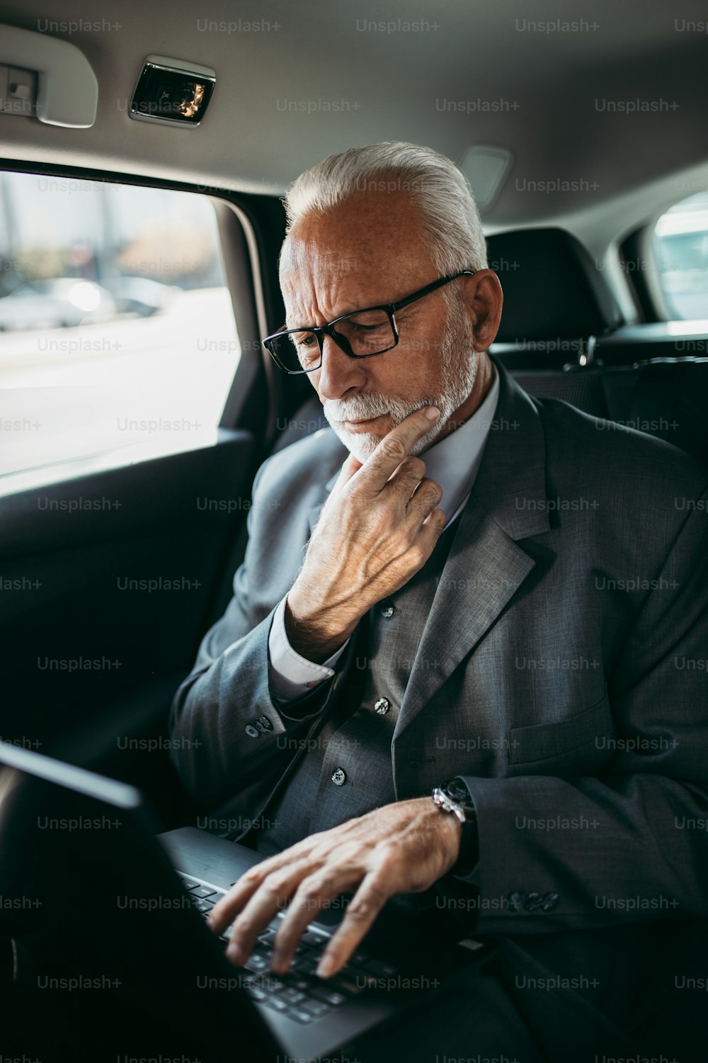 Hombre de negocios senior de buen aspecto sentado en el asiento trasero en un automóvil de lujo. Usando su computadora portátil y reaccionando emocionalmente. El transporte en el concepto de negocio corporativo.