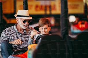 Grand-père et petit-fils s’amusent et passent du temps de qualité ensemble dans le parc d’attractions. Ils s’amusent et sourient tout en conduisant ensemble une auto-tamponneuse.