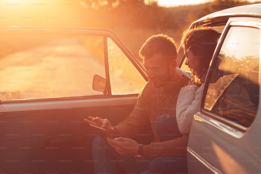 Casal bonito em viagem de carro, eles estão fazendo uma pausa na condução e à procura de direção no tablet.