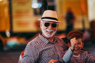 Grandfather and grandson having fun and spending good quality time together in amusement park. They enjoying and smiling while driving bumper car together.