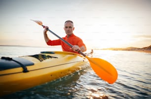 Active senior man paddling the kayak on a sunset sea.