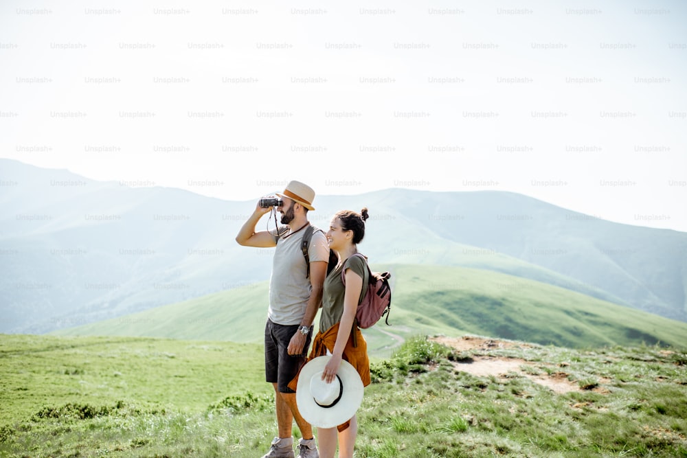 Couple enjoying beautiful landscape views, while traveling with backpacks in the mountains during the summer vacations