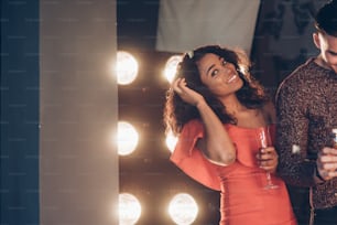 Beautiful afro american young girl in red dress looking to the camera and smiling while walking with friend and holding the glass of drink.