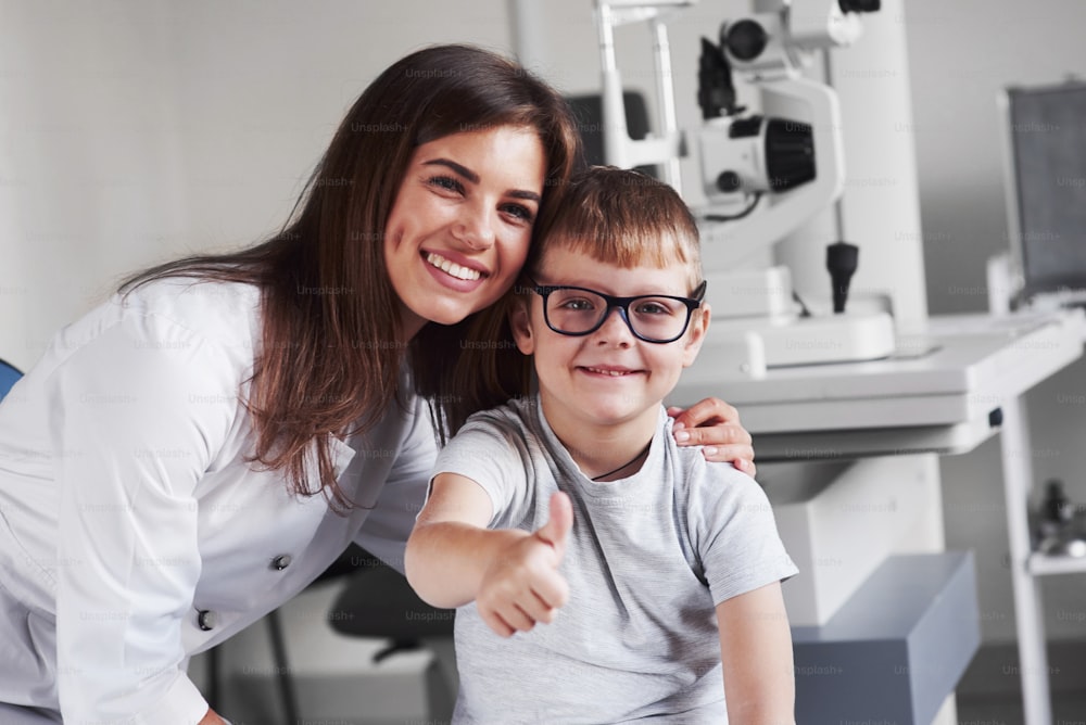 Attractive female blonde young doctor smiling with her satisfied little patient. Glasses are perfectly selected.