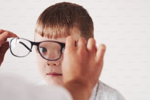 Divirtiendo. El médico le da al niño unas gafas negras nuevas para su visión.