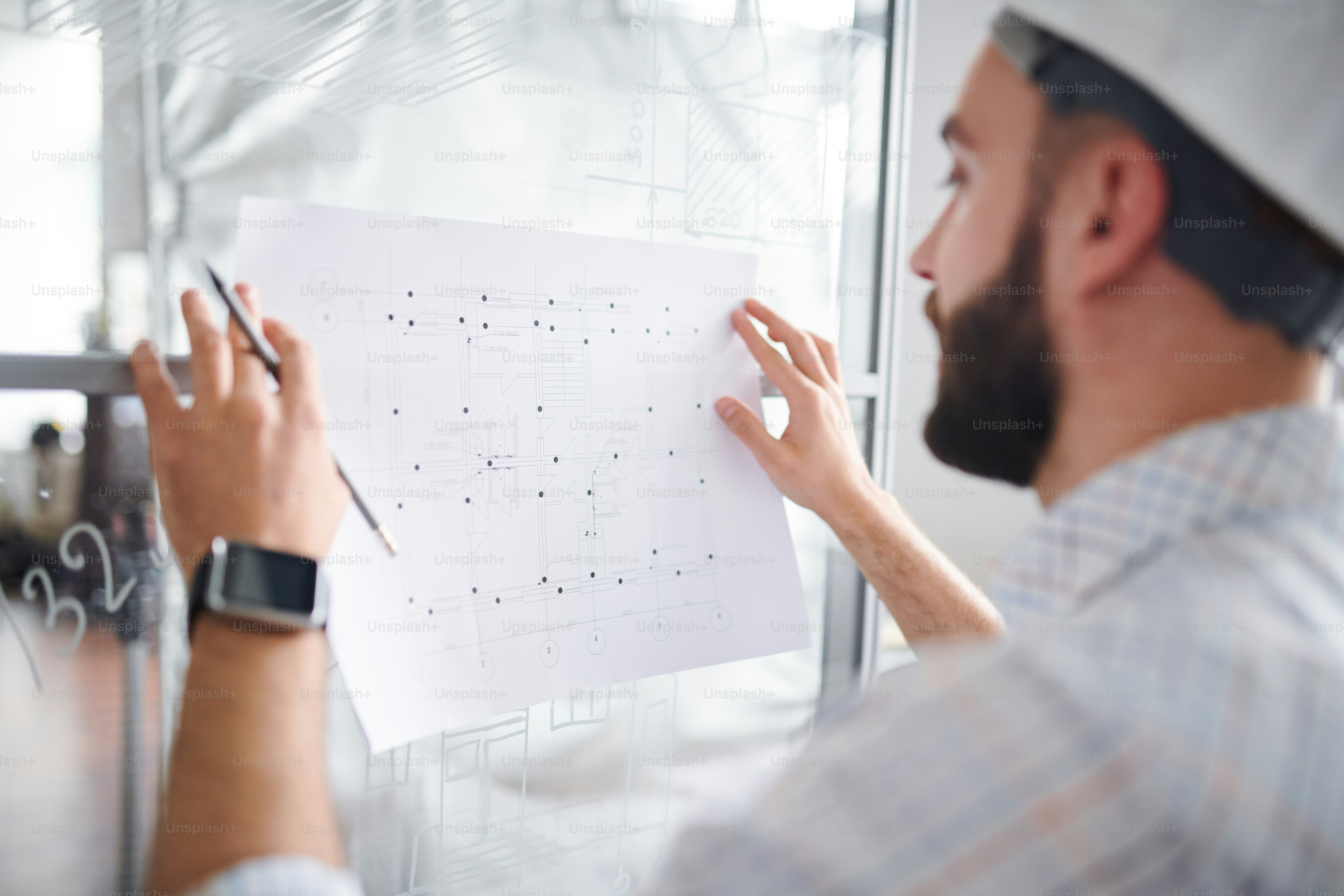 Contemporary engineer or architect standing by board and working over new sketch of construction in office